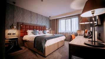 Habitación de hotel con una cama grande, un escritorio, una silla, una lámpara y una ventana con cortinas.