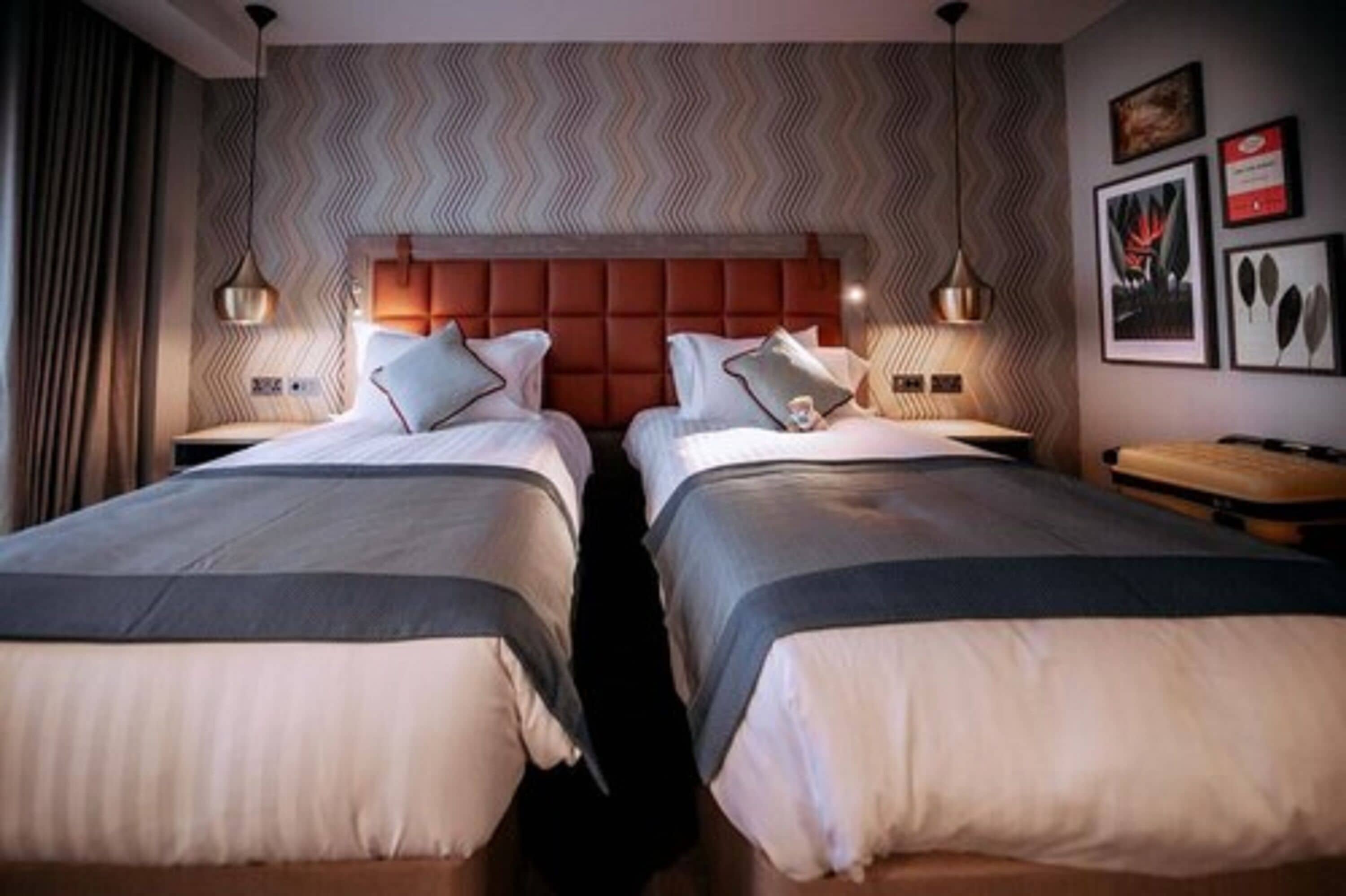 A hotel room with two beds, a chevron-patterned headboard, and framed artwork on the wall.