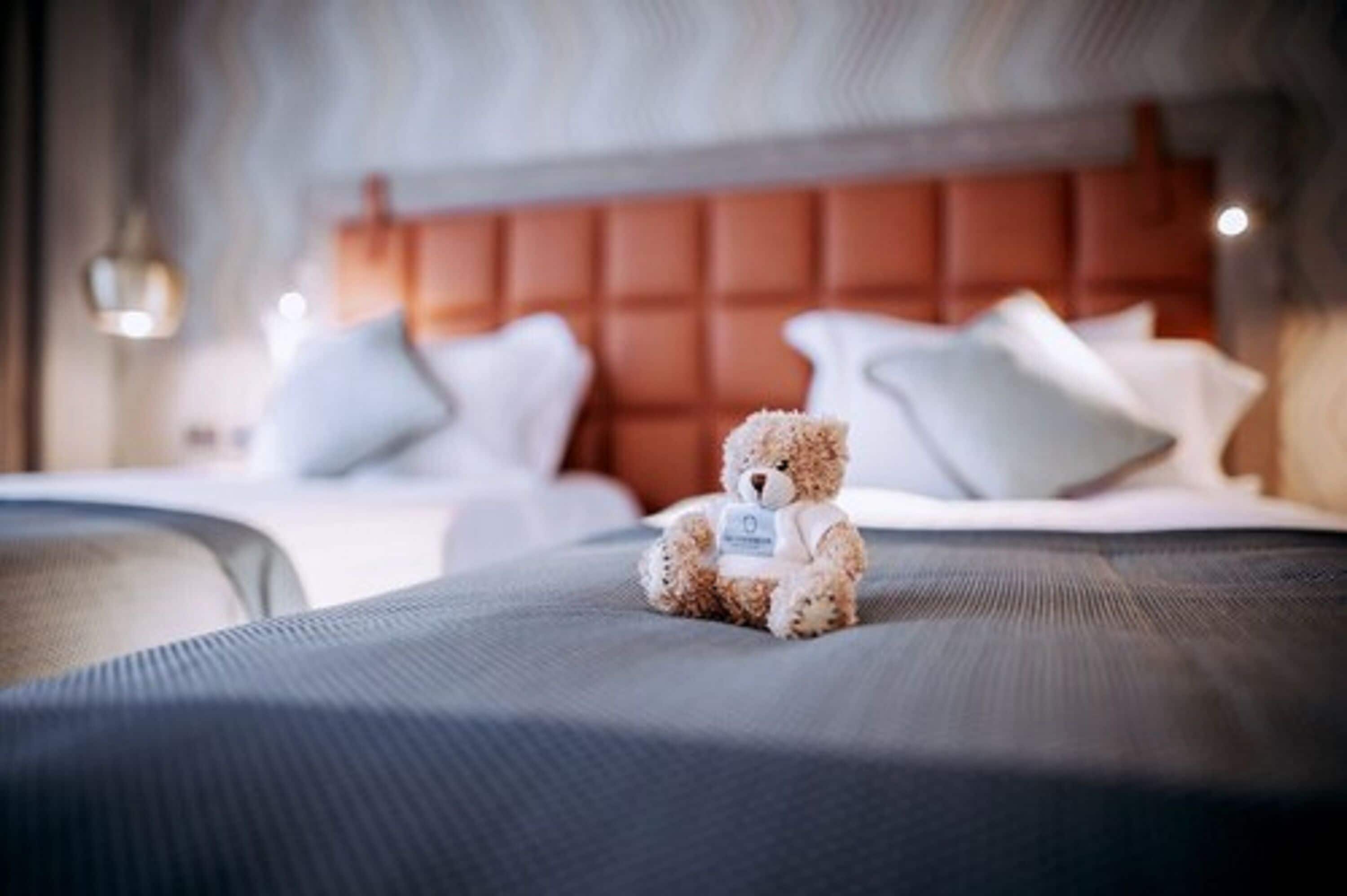 A plush teddy bear on a bed with a headboard and pillows.