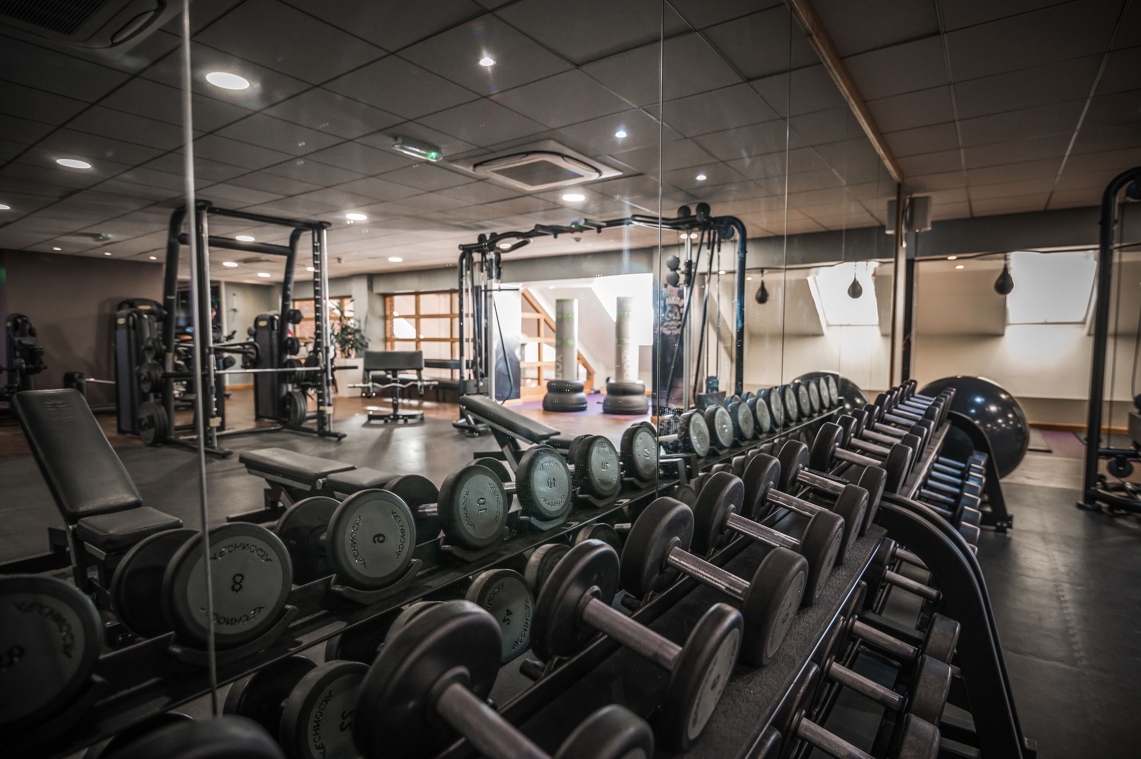 Un gimnasio con diverso equipo de levantamiento de pesas, incluyendo mancuernas y bancos.