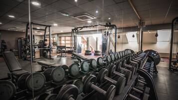 Un gimnasio con diverso equipo de levantamiento de pesas, incluyendo mancuernas y bancos.