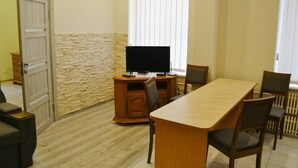 Ein Zimmer mit einem Holzesstisch, Stühlen, einem Fernseher auf einer Kommode, einer Wand mit Steinakzenten und einer Tür.