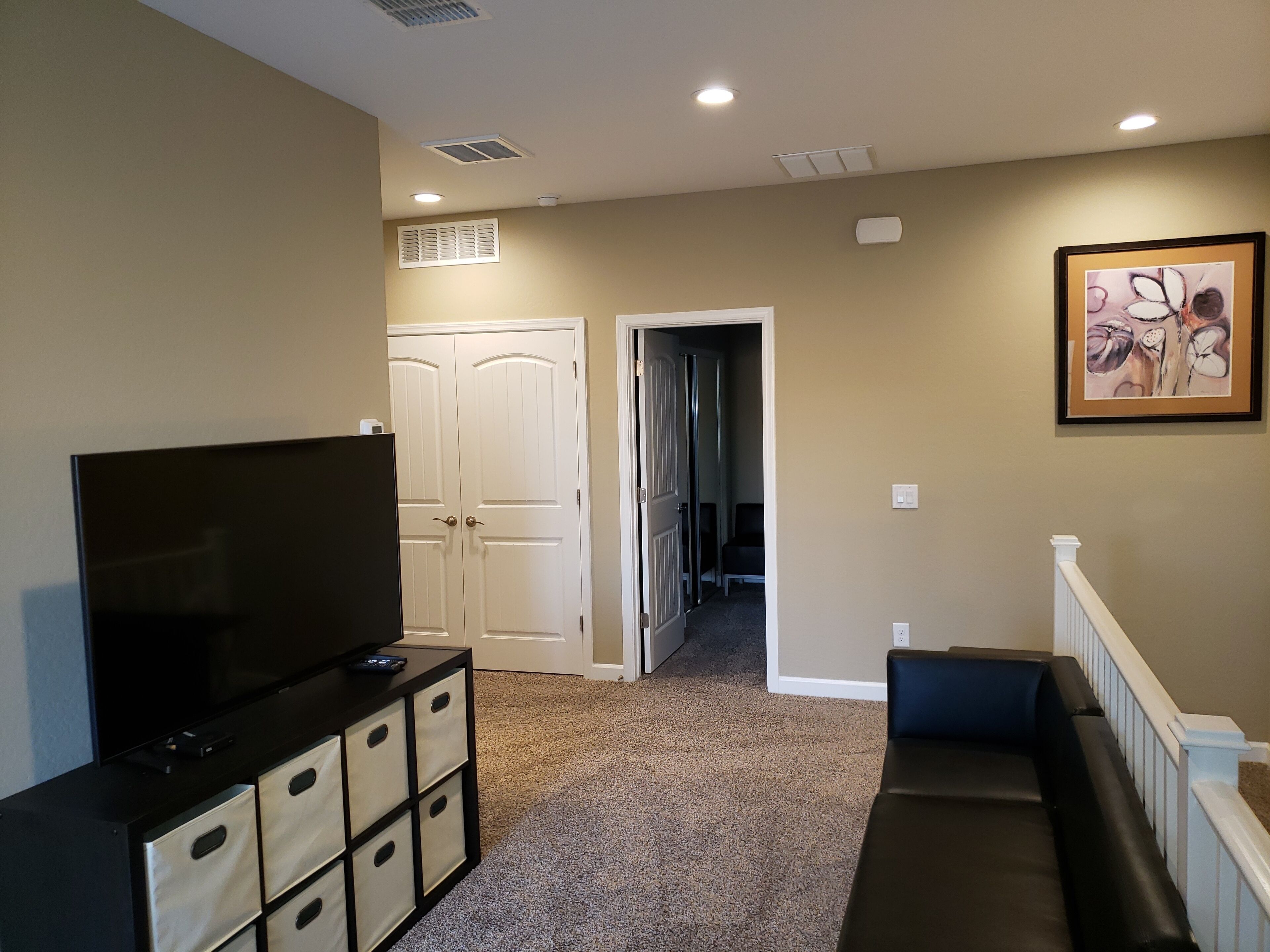 A hallway with beige walls, a white door, a framed picture, and a black entertainment unit.