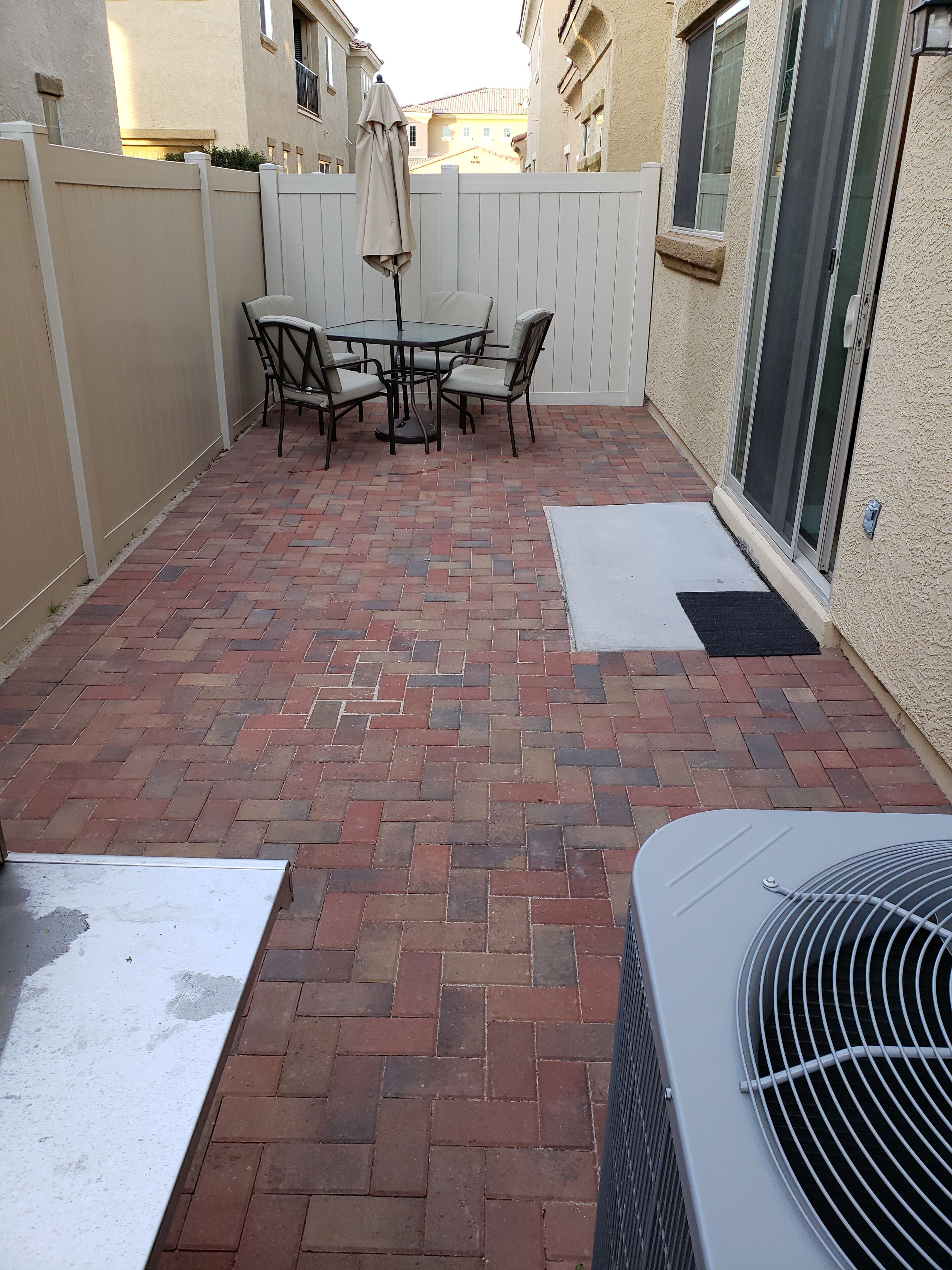 A patio with a brick floor, a table with chairs, and a covered area.