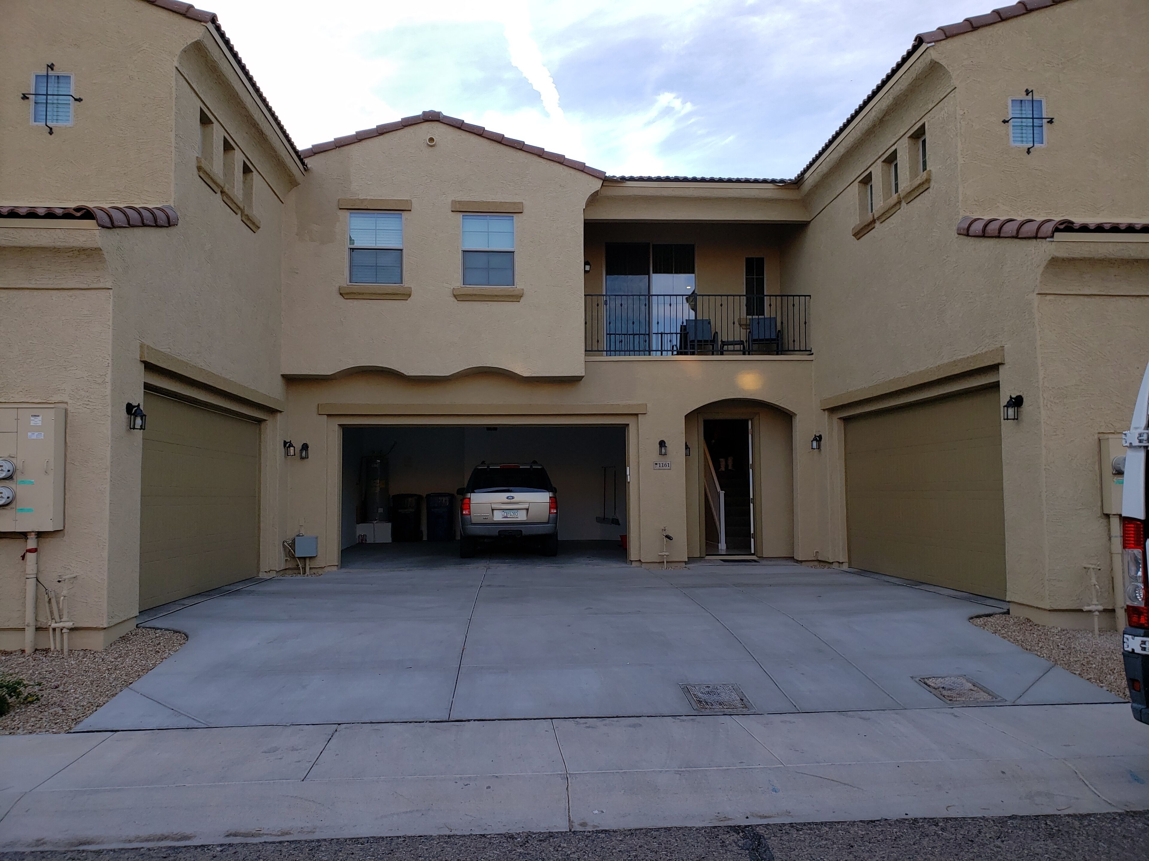 A two-story residential building with a garage entrance, a balcony on the upper floor, and a vehicle parked inside.