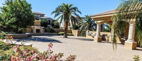 A courtyard with palm trees, a pergola, and a paved walkway.