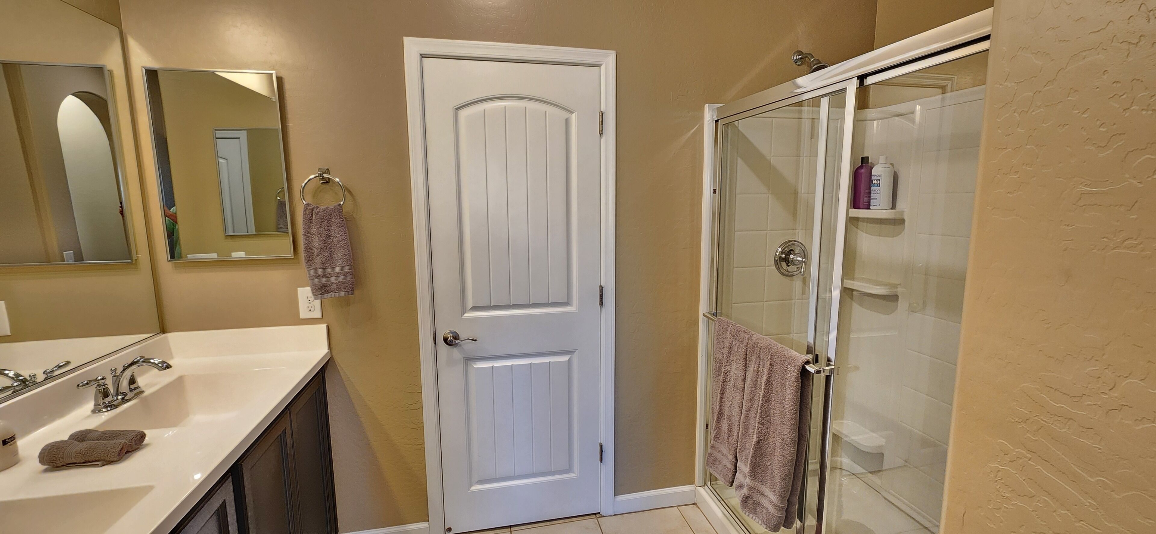 A bathroom with a white door, a glass shower enclosure, and a sink with a towel.