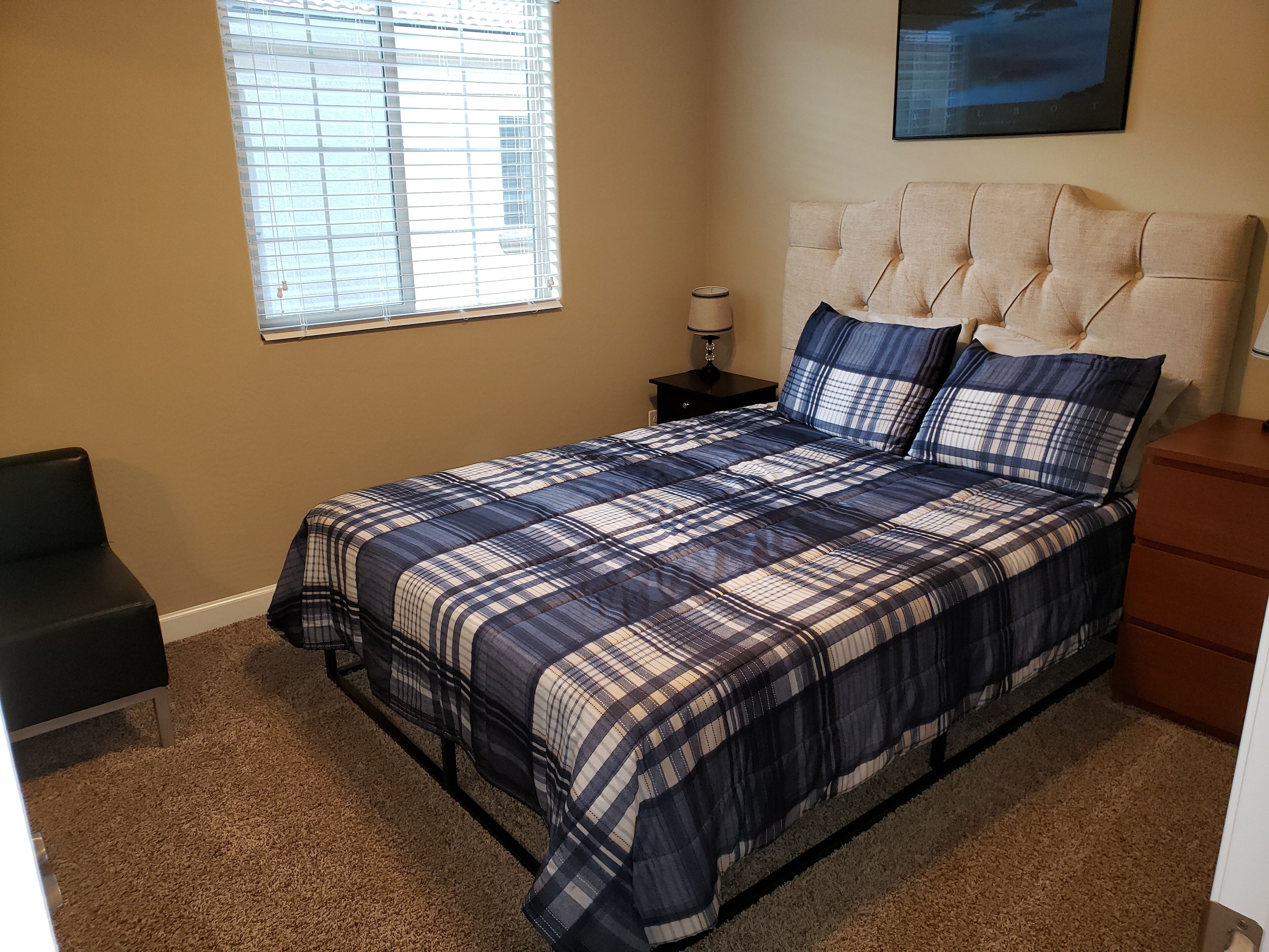 A bedroom with a bed, a nightstand, a lamp, a chair, and a window with blinds.