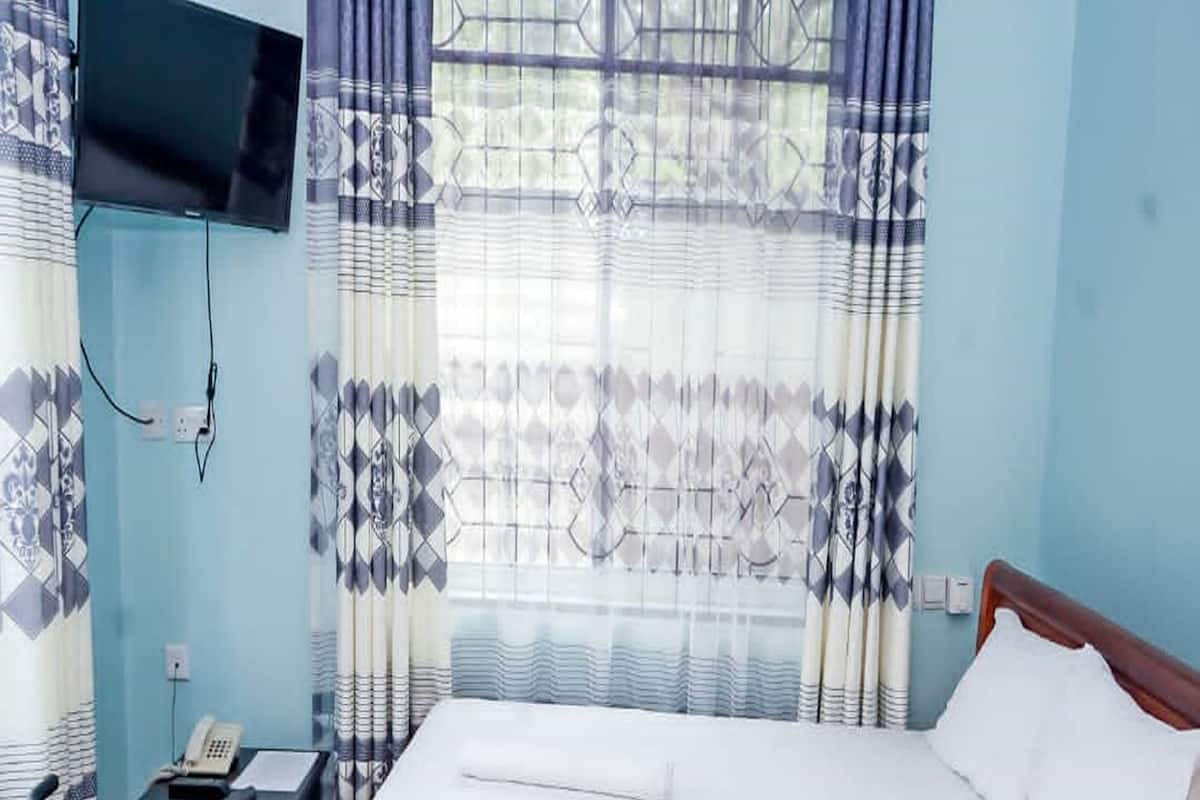 Ein Hotelzimmer mit einem Bett, einem Schreibtisch mit Telefon und einem an der Wand befestigten Fernseher.