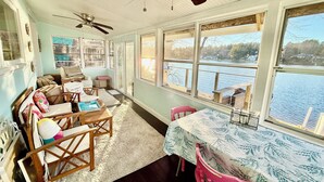 A cozy room with a large window overlooking a lake, furnished with a sofa, chairs, and a dining table. - Your Cottage on the Lake (Dudley)