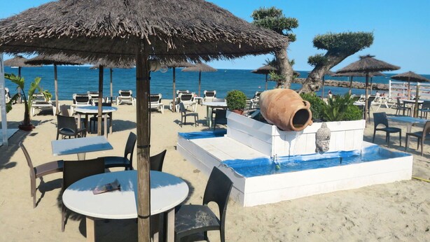 A beachside restaurant with thatched umbrellas, outdoor seating, and a water feature. - Cosy apartment for 3 guests with WIFI, A/C, TV, balcony and pets allowed (Saint-cyprien-plage)