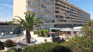 A multi-story hotel with balconies, a palm tree, and outdoor seating area. - Cosy apartment for 3 guests with WIFI, A/C, TV, balcony and pets allowed (Saint-cyprien-plage)