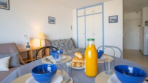 A dining table set with blue bowls, plates, and a bottle of orange juice, with a sofa and a lamp in the background. - Cosy apartment for 3 guests with WIFI, A/C, TV, balcony and pets allowed (Saint-cyprien-plage)