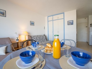 Una mesa de comedor dispuesta con cuencos azules, platos y una botella de jugo de naranja, con un sofá y una lámpara al fondo.