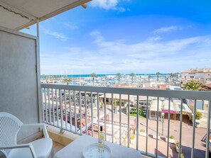 Un balcon avec une table et des chaises, donnant sur une marina où l’on peut admirer des bateaux et des bâtiments.