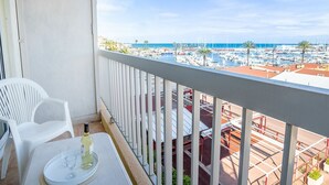 A balcony with white chairs, a table with a bottle and glass, and a view of a marina with boats and palm trees. - Cosy apartment for 3 guests with WIFI, A/C, TV, balcony and pets allowed (Saint-cyprien-plage)
