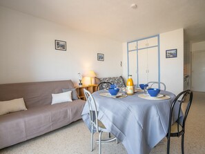 Un salon chaleureux avec un canapé, une table à manger dressée avec des bols et des assiettes bleus, et une lampe sur une table d’appoint.