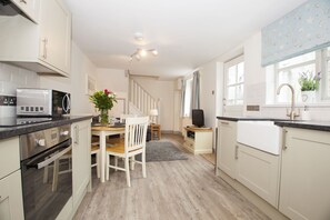 A modern kitchen with white cabinetry, a built-in oven, a microwave, and a dining area with a wooden table and chairs.