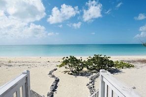 A beach with a wooden walkway leading to the water, surrounded by greenery. - Private Beach front cottage (Old Bight Settlement)