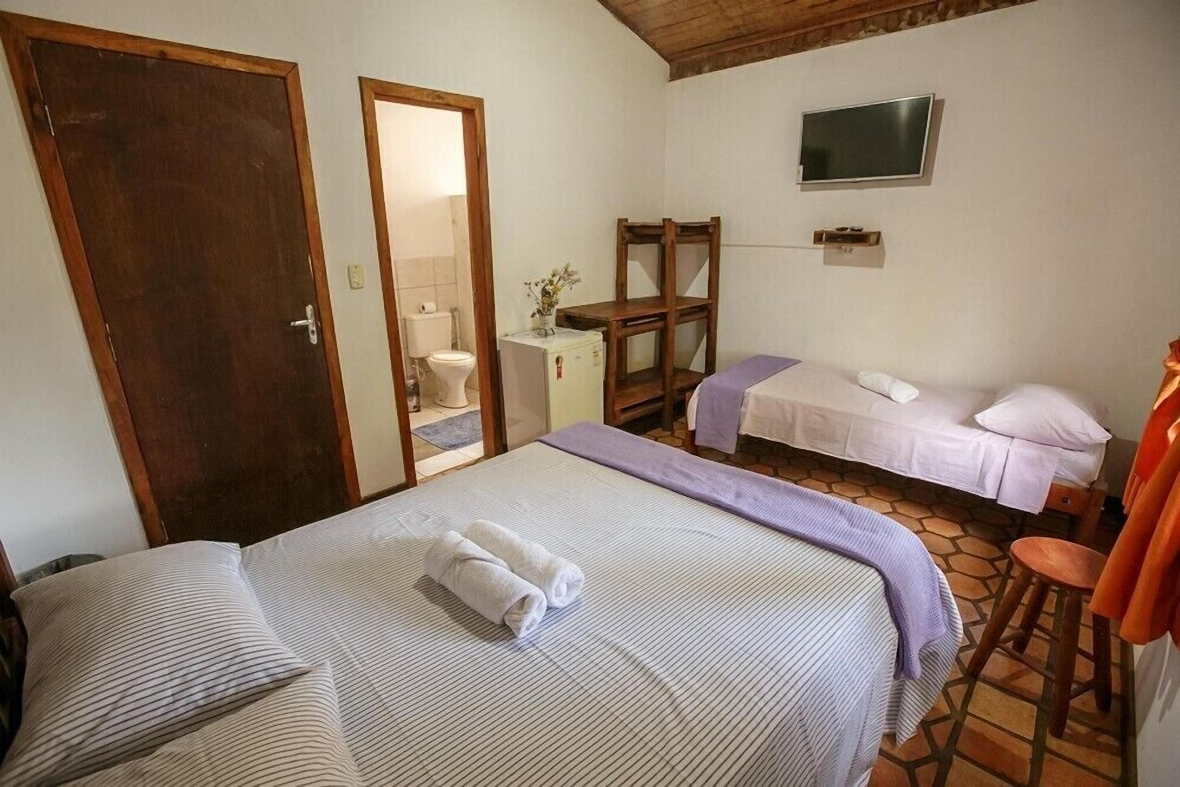 Une chambre avec deux lits, une télévision, une armoire en bois et une salle de bain visible par une porte ouverte.