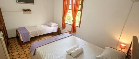 A room with two beds, a small table, a TV mounted on the wall, and a window with curtains.
