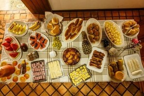 A table with various food items including fruits, pastries, and meats. - Pousada Casa de Jorge (Lençóis)