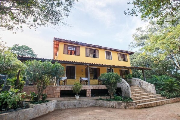A two-story yellow building with a tiled roof, a stone staircase, and a covered patio area with potted plants. - Pousada Casa de Jorge (Lençóis)