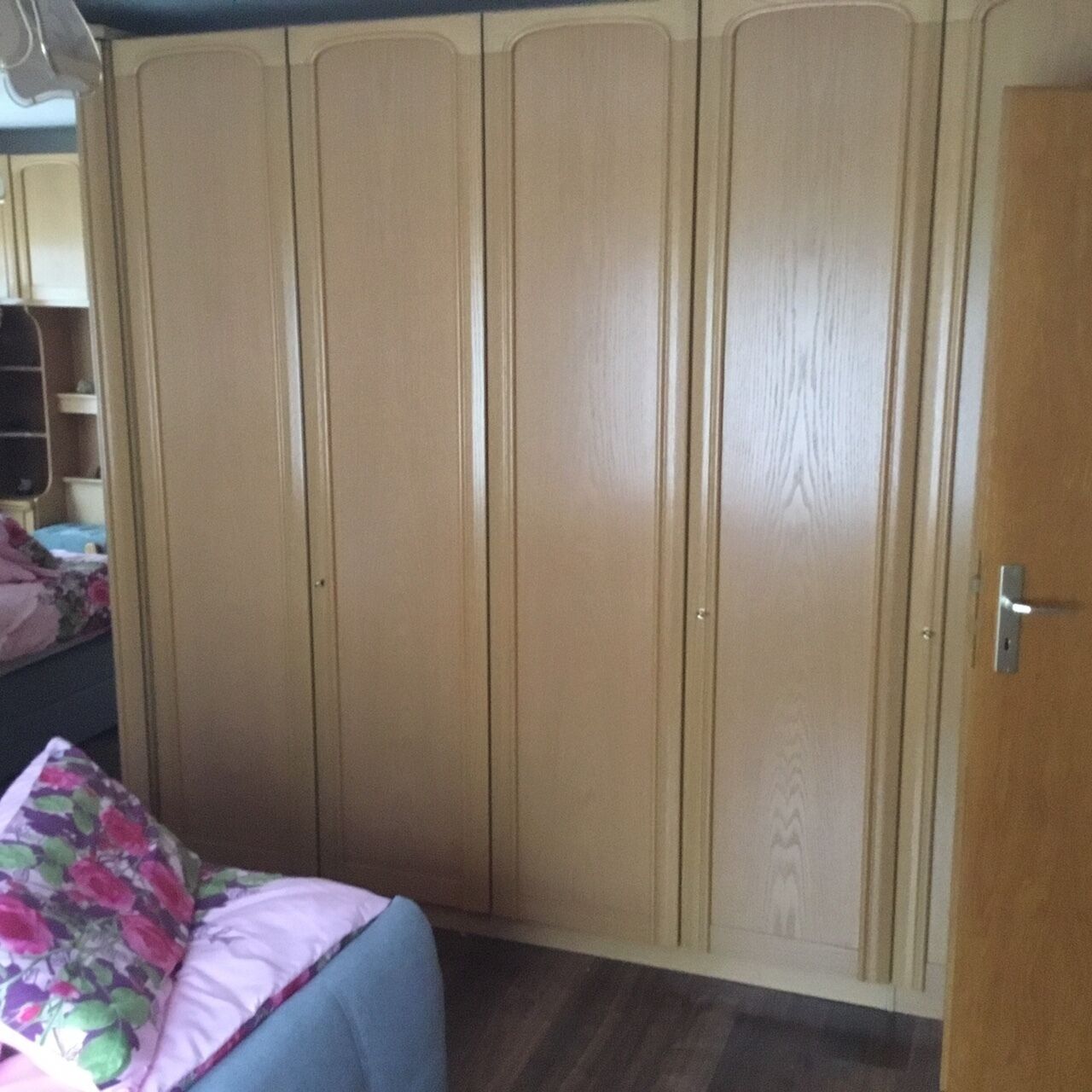 Une chambre avec une grande armoire, un lit agrémenté d’un coussin à motifs floraux et un plancher en bois.