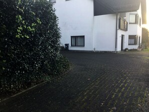 Ein gepflasterter Weg führt zu einem weißen Gebäude mit einem kleinen Fenster und einer Tür.