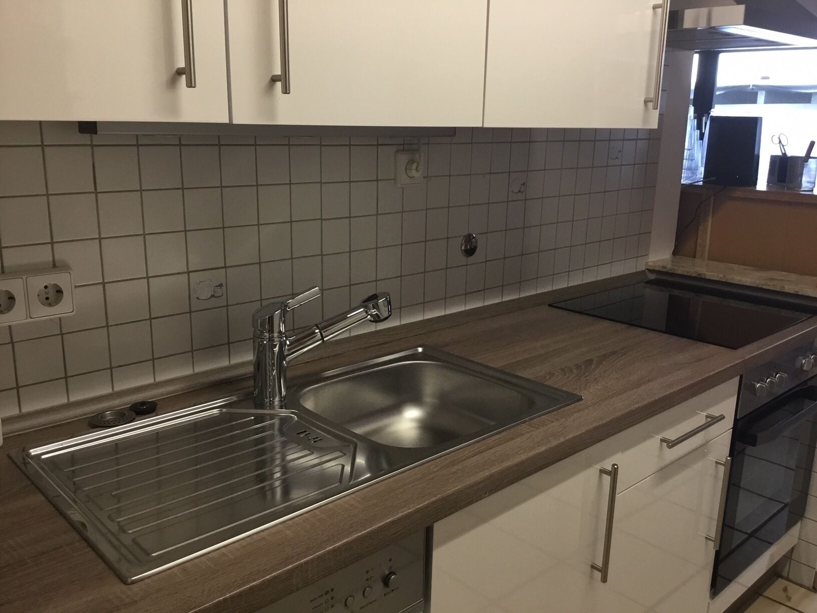 Una cocina con un lavamanos de acero inoxidable, horno empotrado y encimera de madera.