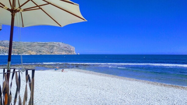 A beach with a white umbrella and a rocky cliff in the background. - House - Sleeps 4 - Pool (Denia)