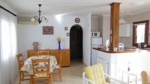 A dining area with a wooden table and chairs, a kitchen with a microwave, and a wooden pillar. - House - Sleeps 4 - Pool (Denia)