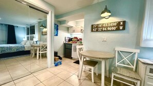 Zona pranzo con tavolo rotondo e sedie, cucina sullo sfondo e parete con bussola che indica le coordinate della stanza.