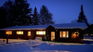 Eine Hütte mit schneebedecktem Dach, einer Veranda und einem beleuchteten Fenster.