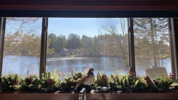 Ein Zimmer mit großem Fenster mit Blick auf einen See, dekoriert mit immergrünen Zweigen und Kiefernzapfen.