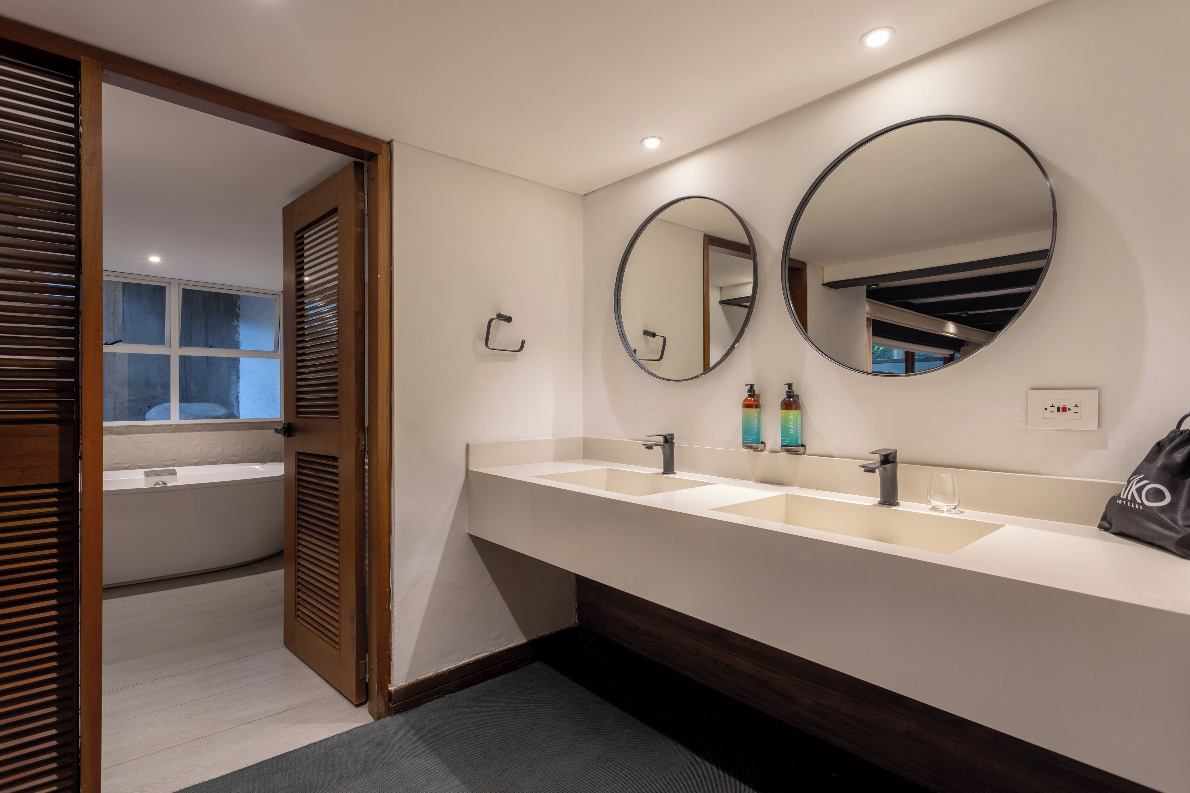 Un baño moderno con un tocador de doble lavabo, dos espejos redondos, una bañera y puertas de madera con listones.