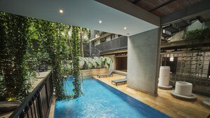 An indoor swimming pool with a wooden deck, lounge chairs, and a view of a lush garden. - Alko Hotel Casa Nispero (Cali)