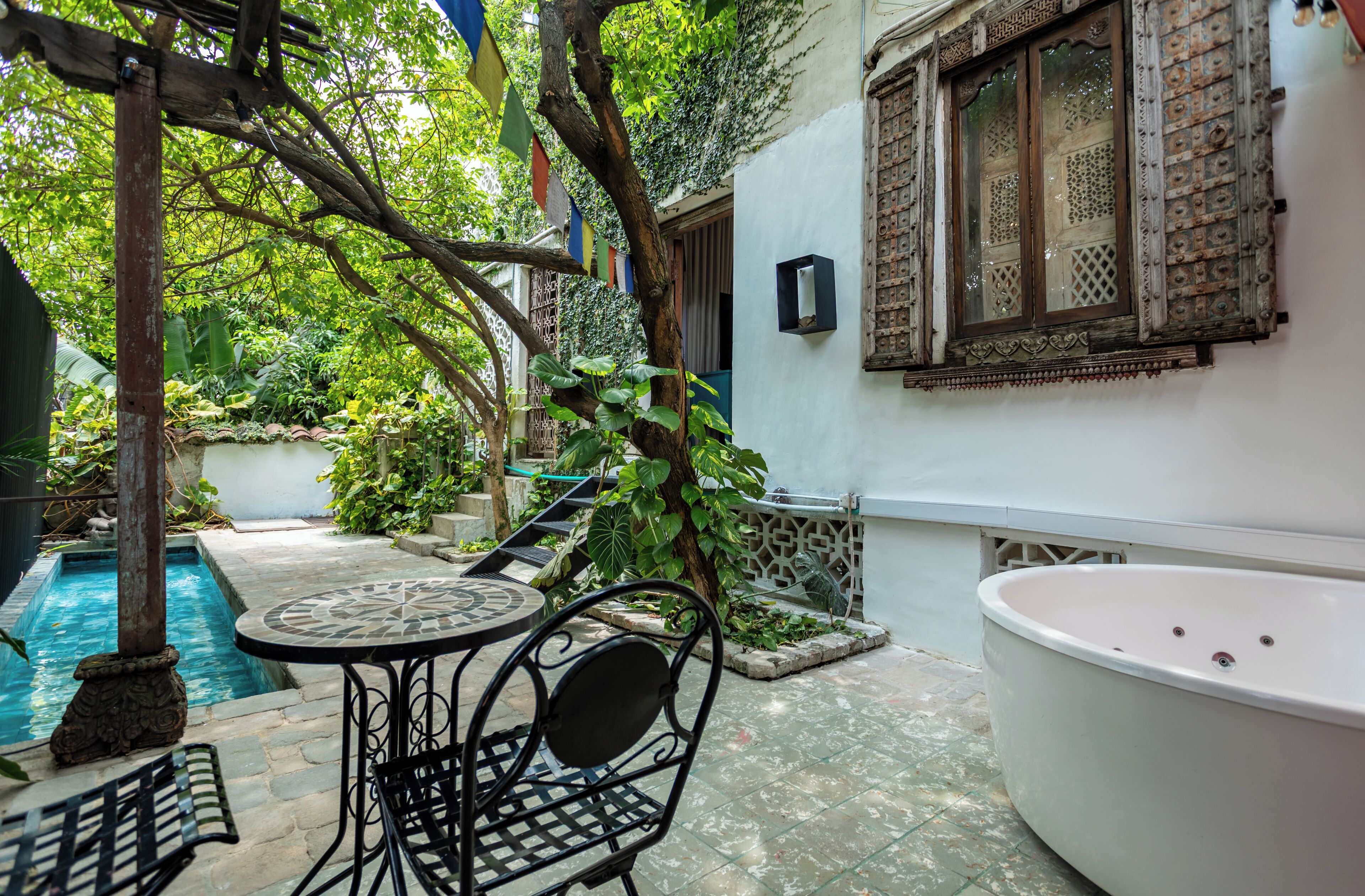A private pool area with a table and chairs, surrounded by lush greenery and a decorative window.