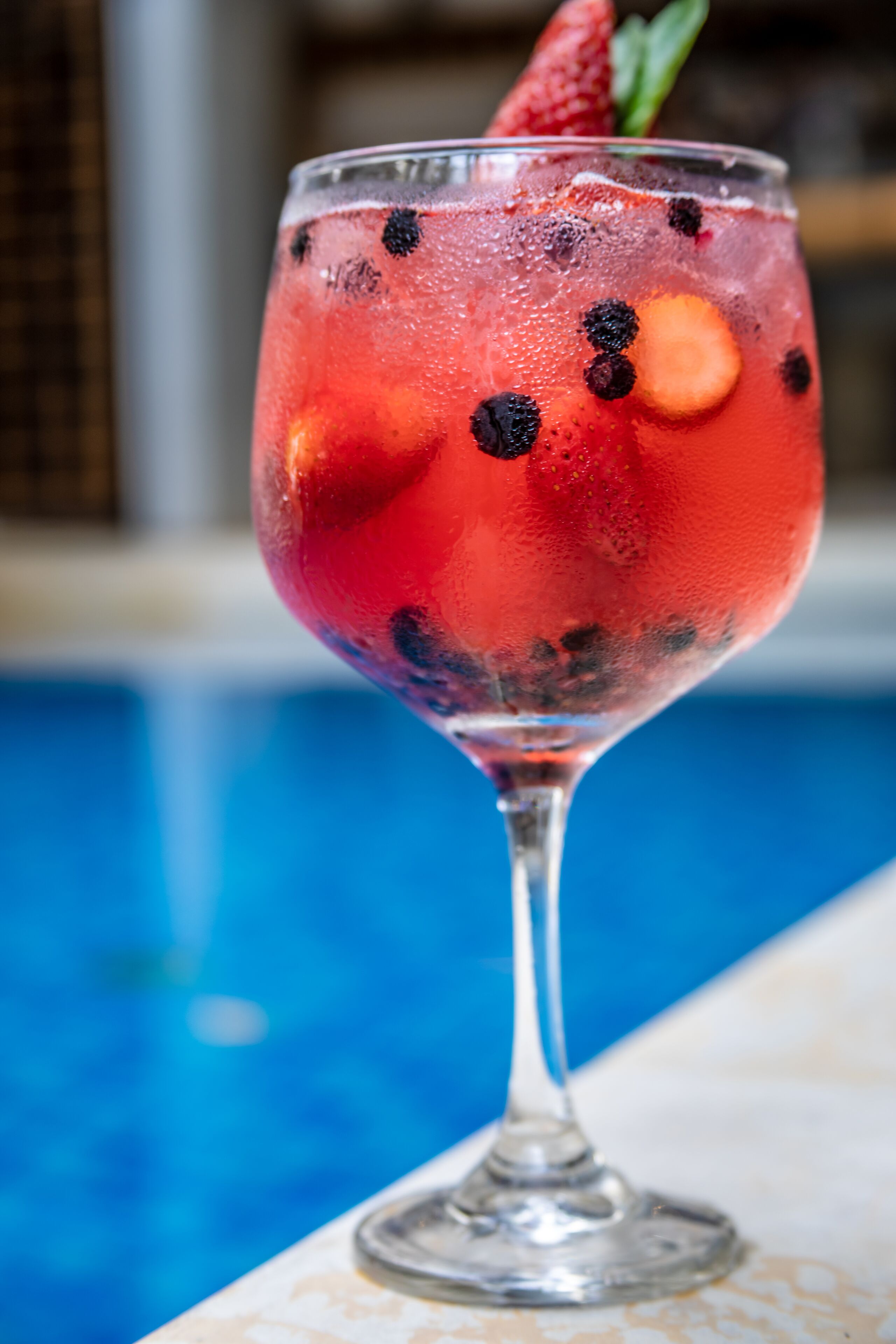 Un vaso de cóctel con fresa y frambuesas, sobre una mesa junto a la piscina.