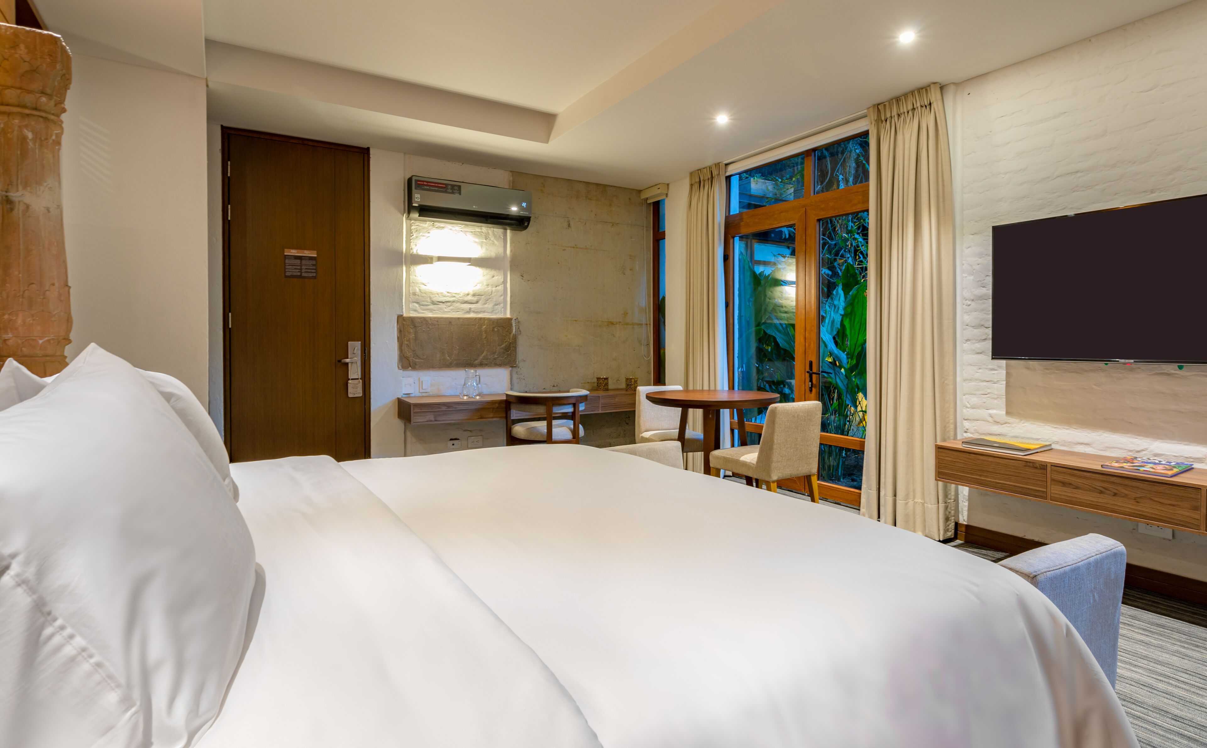 Hotelkamer met groot bed, bureau met stoel, klein tafeltje, televisie en raam met gordijnen.