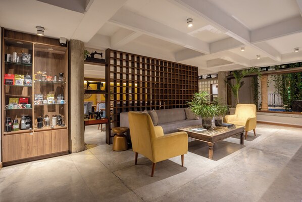 Una sala de estar moderna con un sofá, dos sillones, una mesa de centro y una estantería de madera que exhibe varios objetos.