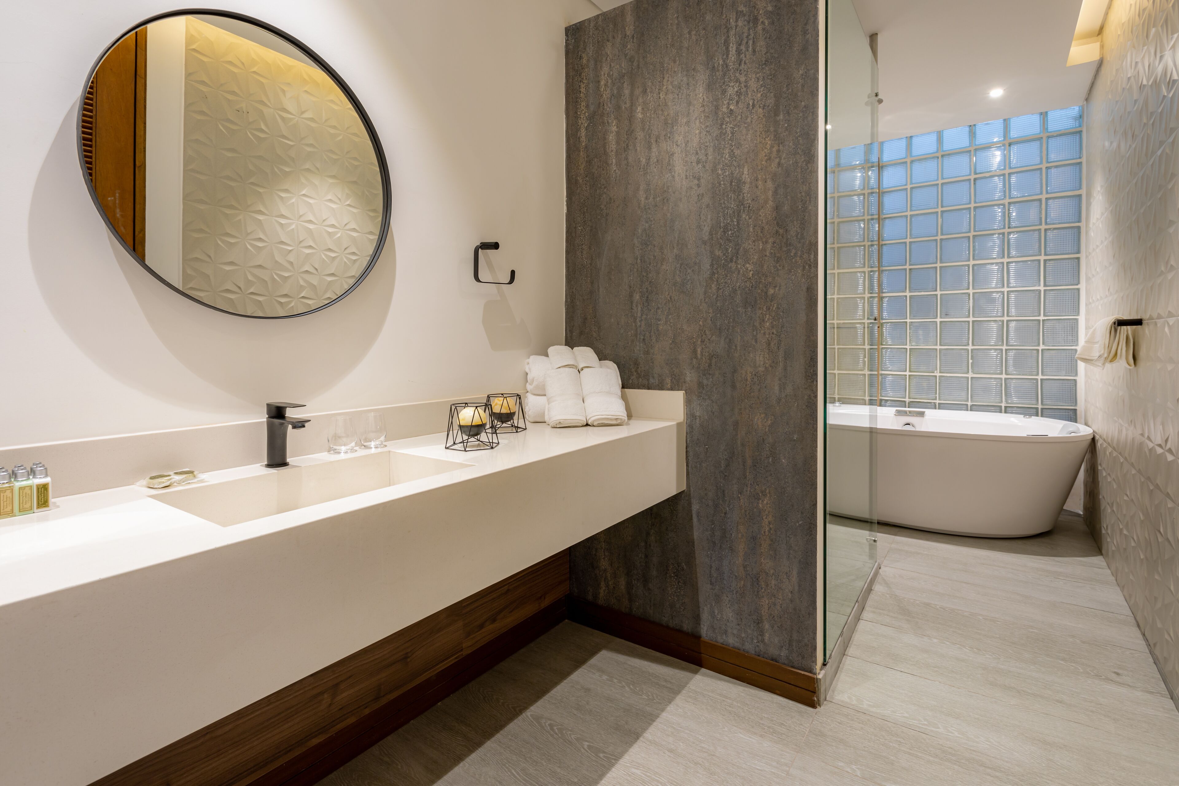 Un baño moderno con un espejo grande, una bañera independiente y un tocador con encimera amplia.