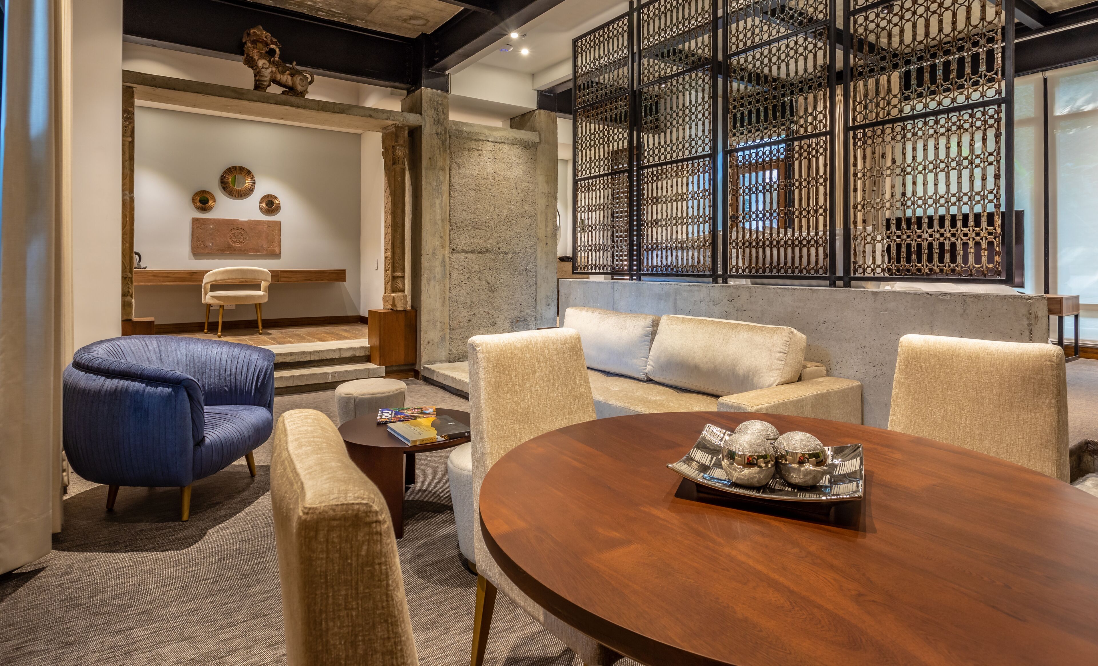 A modern living room with a round wooden table, beige sofas, and a blue armchair.