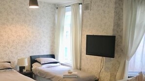 A hotel room with two beds, a flat-screen TV, a sofa, and a window with curtains. - Macleods Guest House (Blackpool)