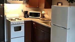 Una cocina compacta con armarios de madera, una estufa blanca, un microondas, un refrigerador y un lavamanos pequeño.