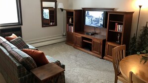 Una sala de estar con sofá, televisor, estantería y una mesita.