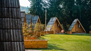A row of wooden cabins with sloped roofs, surrounded by a grassy area and dense trees. - Glamping FOREST EDGE (Kamnik)
