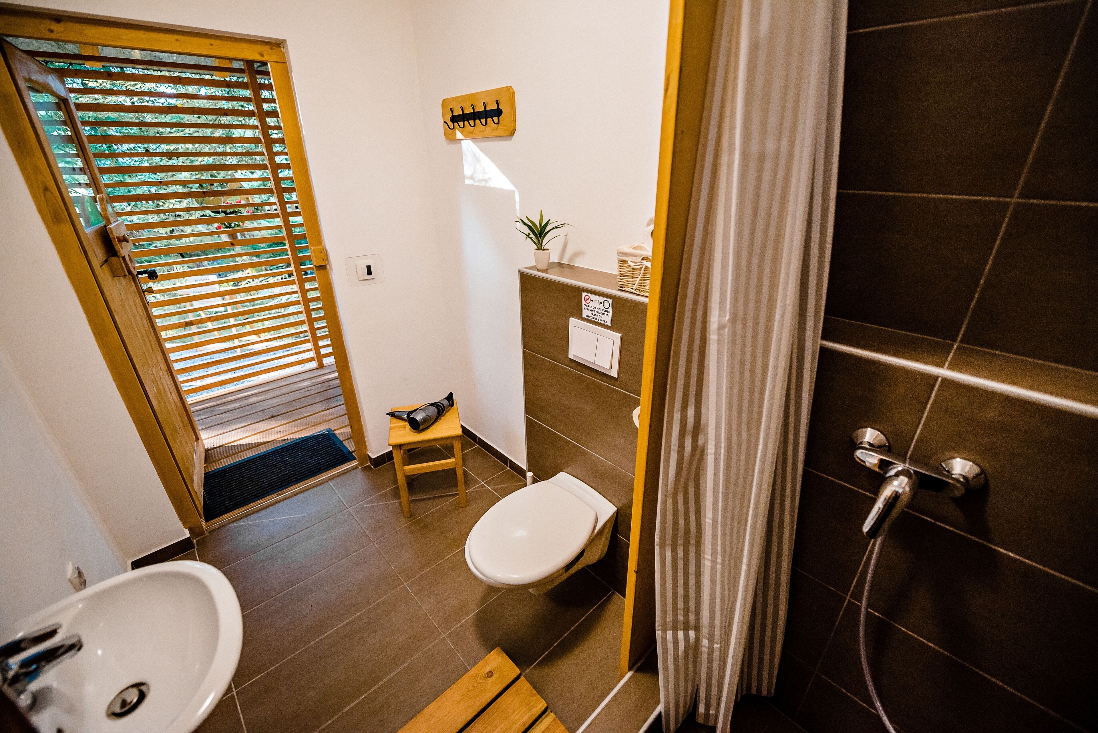 A bathroom with a sink, toilet, shower, and a small wooden stool.