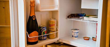 Un mini refrigerador con una botella de champán, una lata de cerveza y un recipiente con yogur.