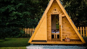 A wooden triangular cabin with a door labeled "RZENIK" and a small wooden bench outside. - Glamping FOREST EDGE (Kamnik)